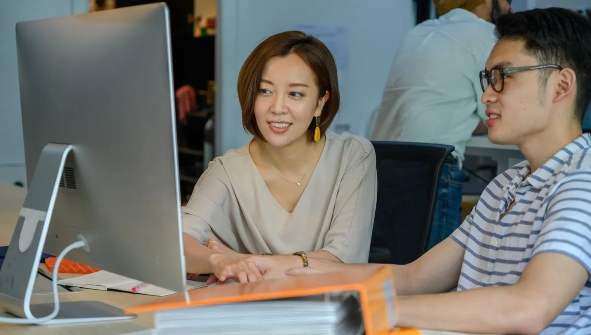 Two colleagues collaborating at a screen in a warm, modern workspace.