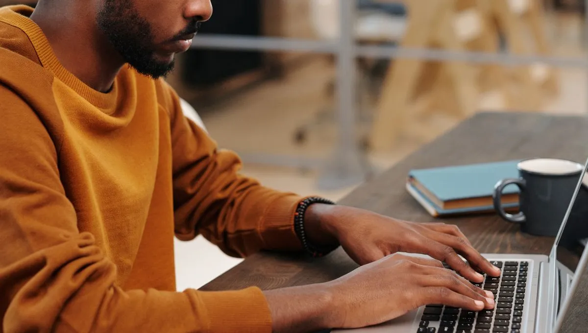 A person in a warm rust sweater working on a laptop in a softly lit office.